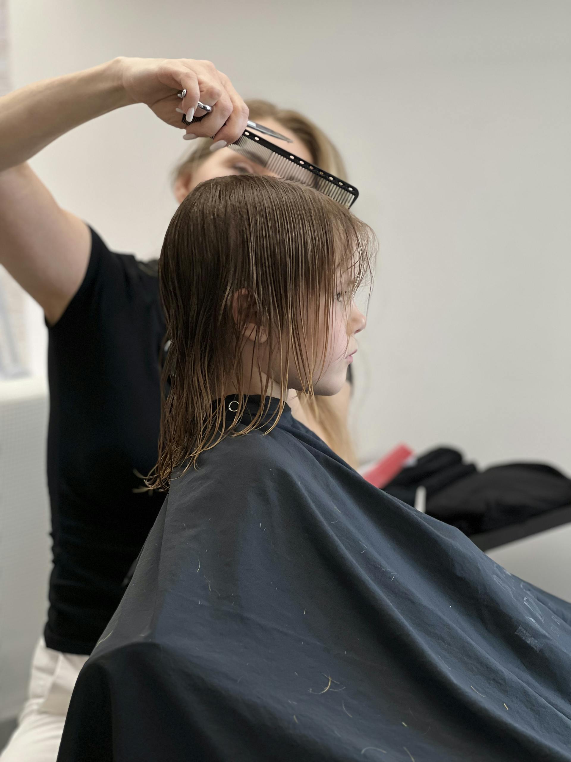 Child getting haircut in salon, focused on stylist's technique and salon environment.