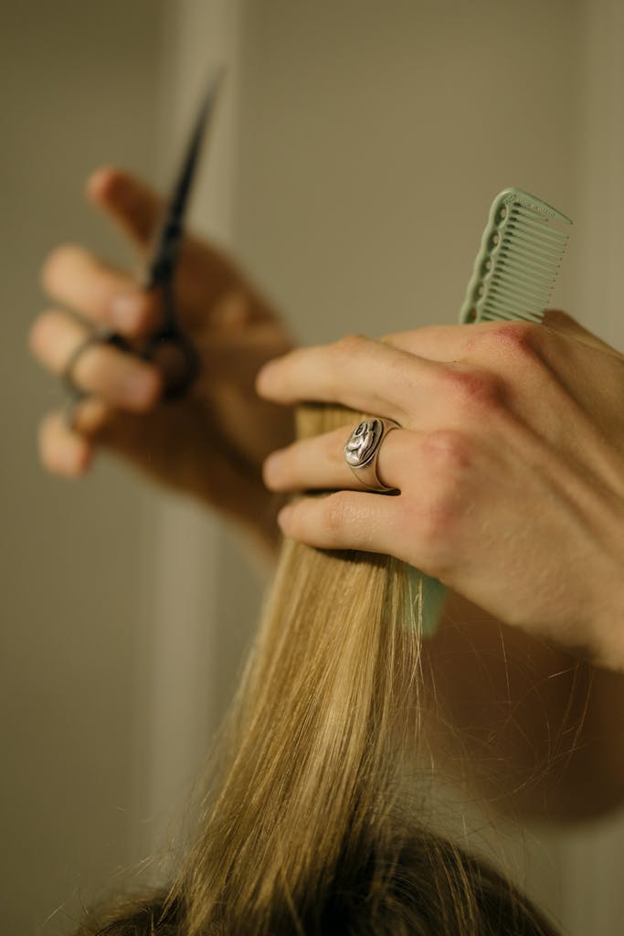 Close-up of a hairdresser trimming blonde hair using scissors and a comb.
