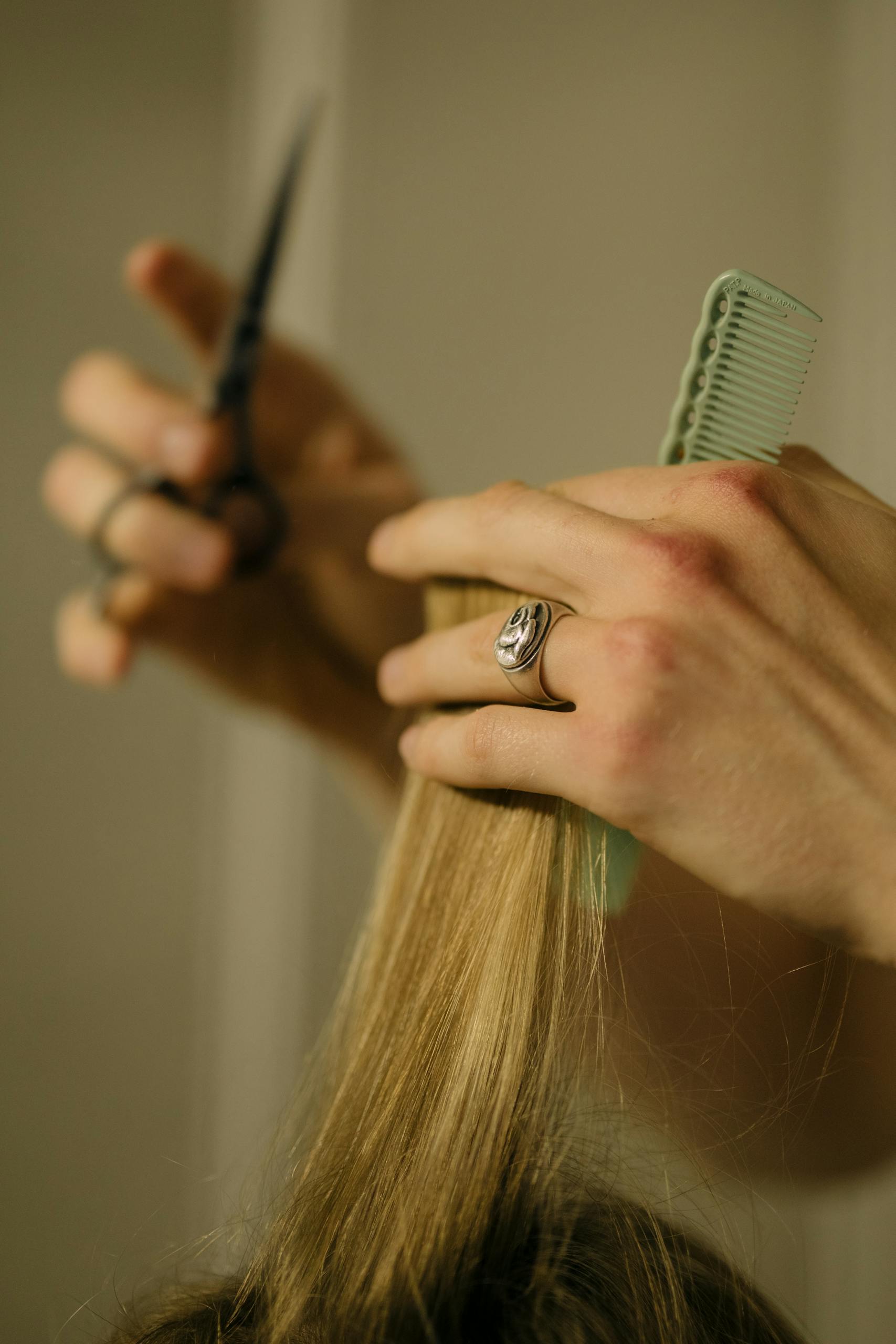 Close-up of a hairdresser trimming blonde hair using scissors and a comb.